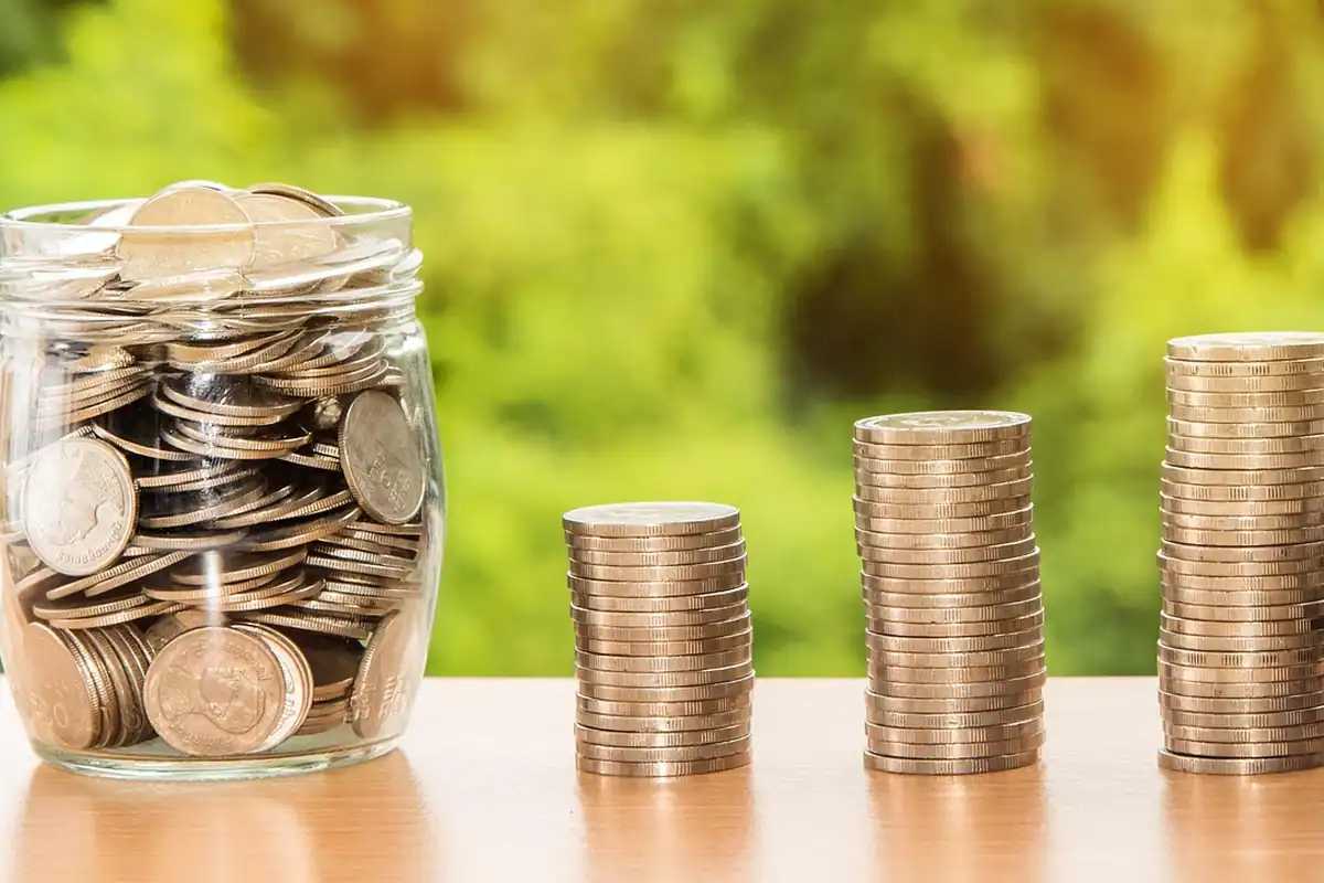 Borcan cu monede și stive de monede pe o masă, simbol al economiilor