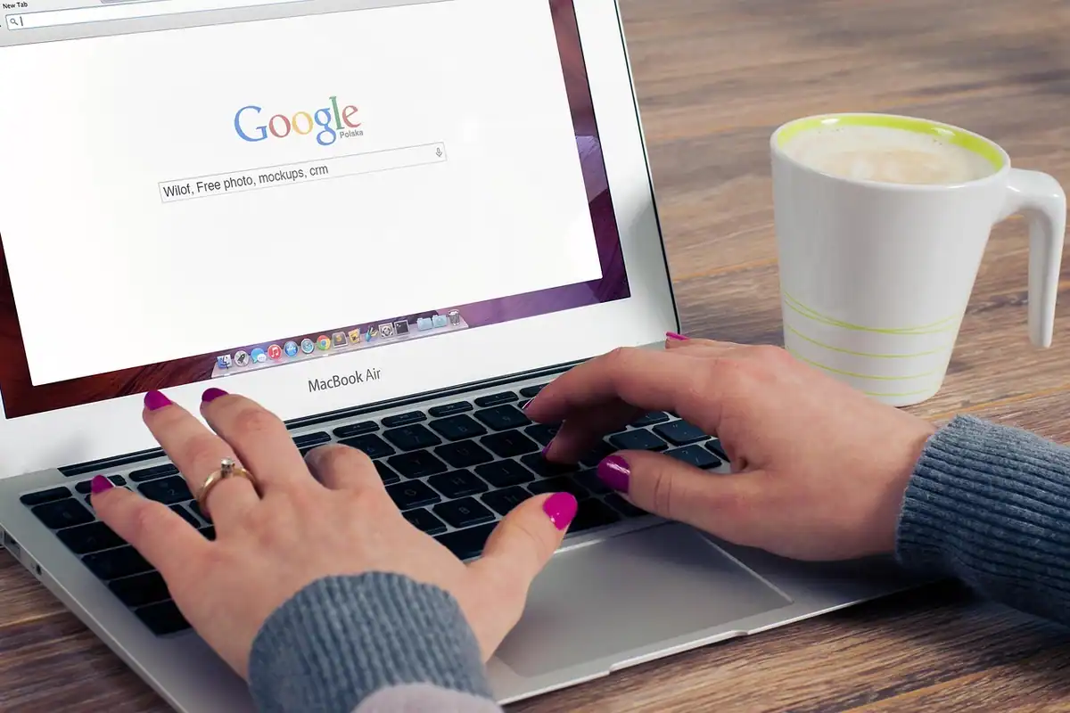 Mâini care tastează pe un laptop cu pagina de căutare Google