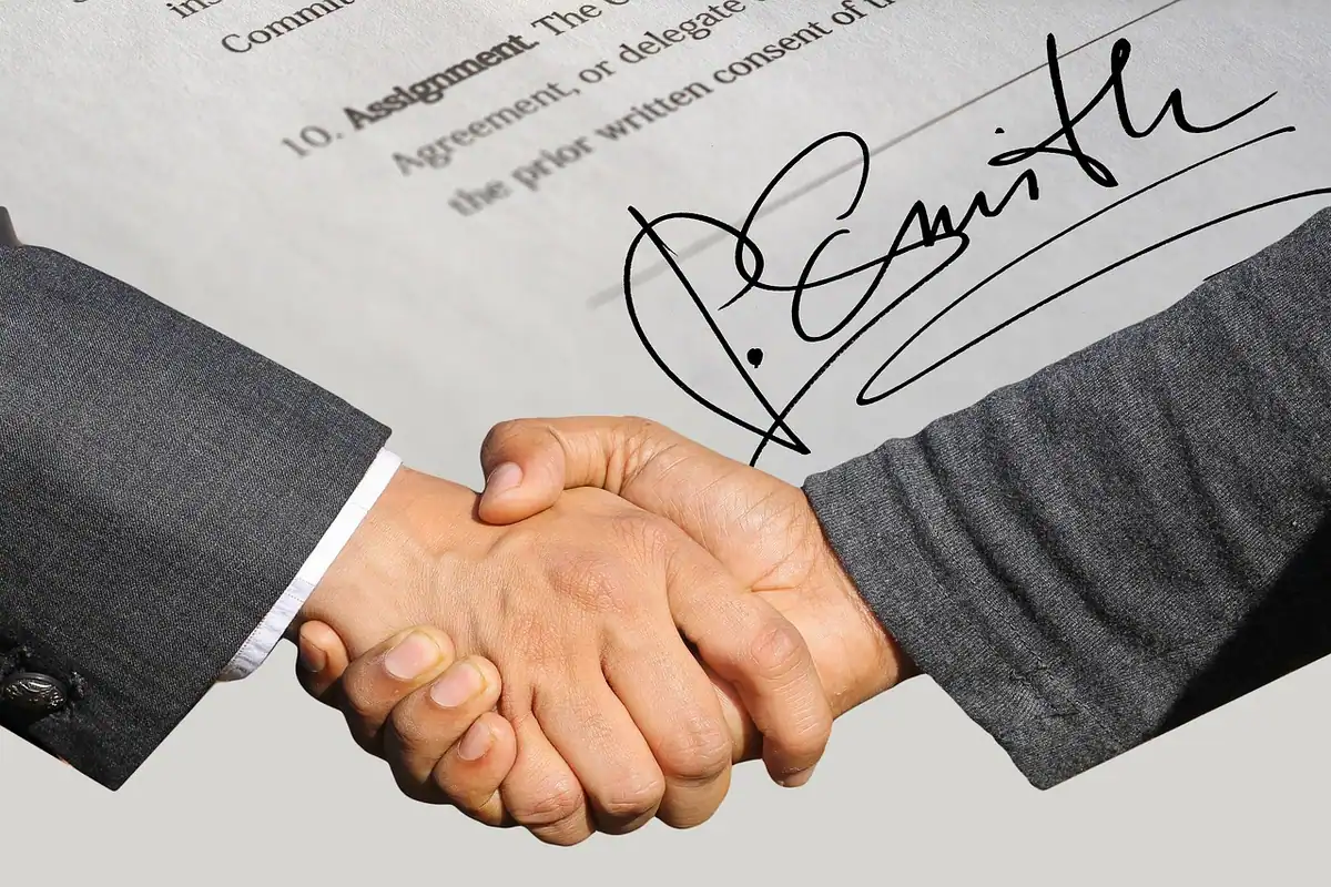 Strângere de mână peste un contract semnat, simbol al unei colaborări