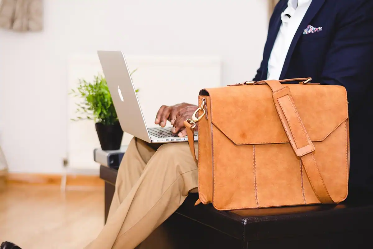 Bărbat cu laptop pe genunchi și o geantă din piele maro lângă el