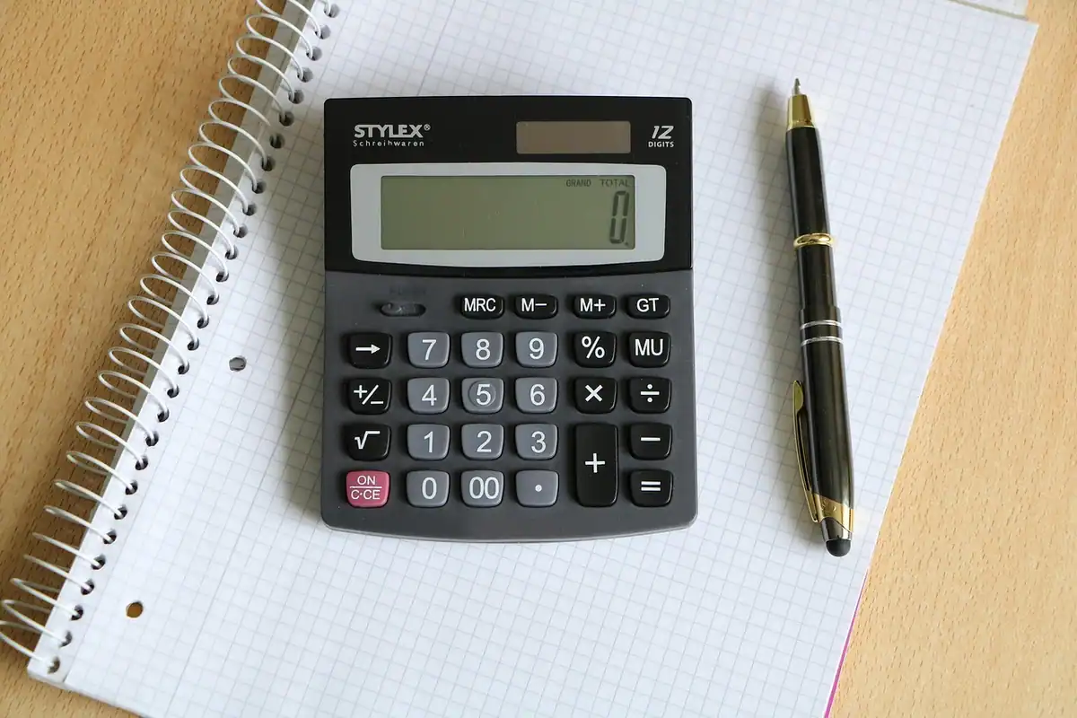 Calculator de birou și pix așezate pe un caiet cu spirală