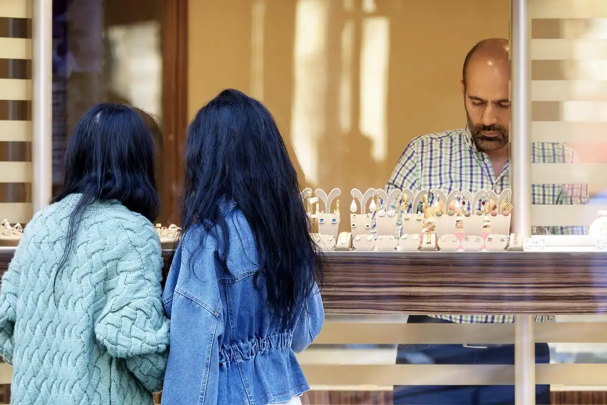 Două tinere în fața unei vitrine, iar în spate vânzătorul din magazin