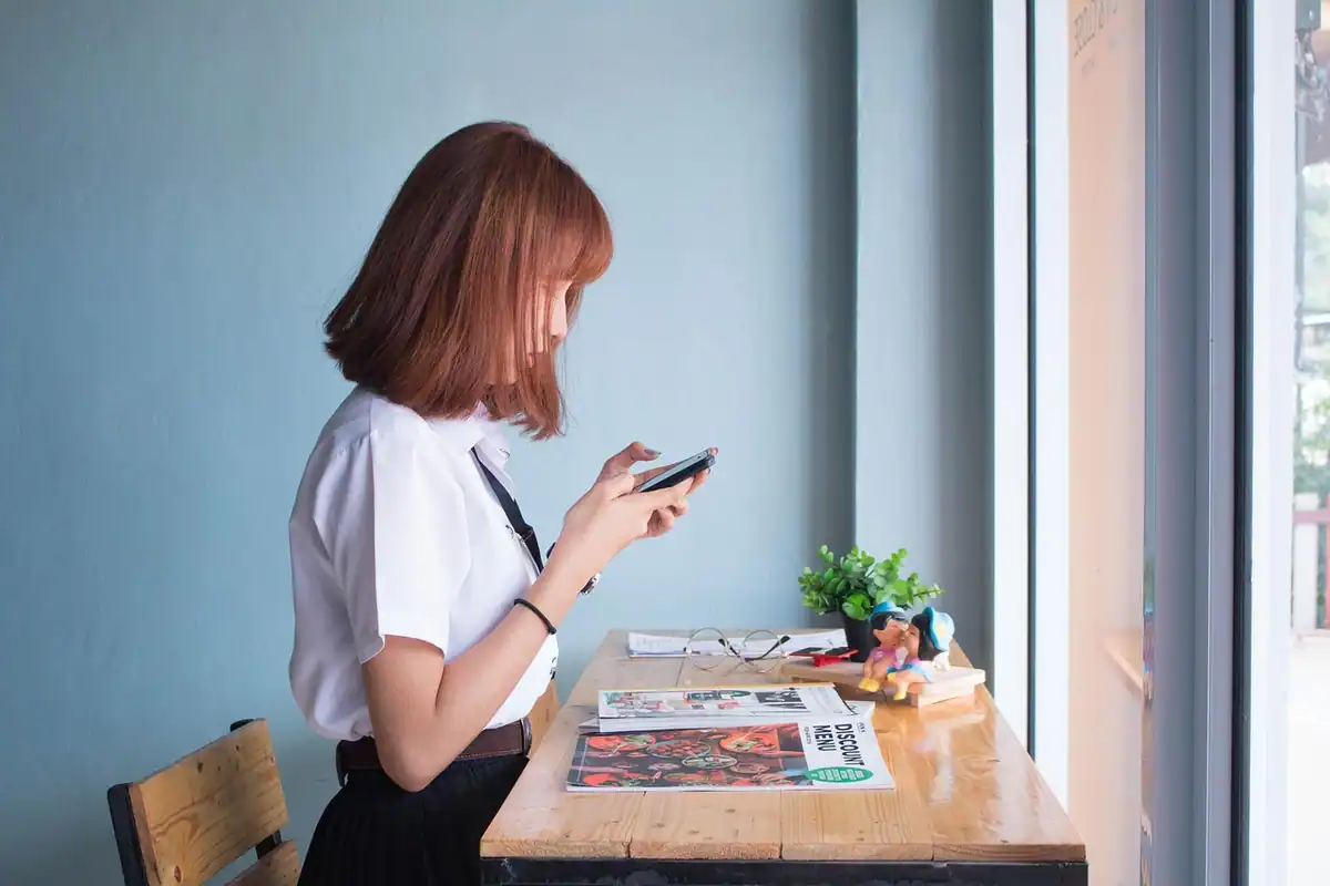 Tânără care citește pe telefon, lângă o masă de la fereastră