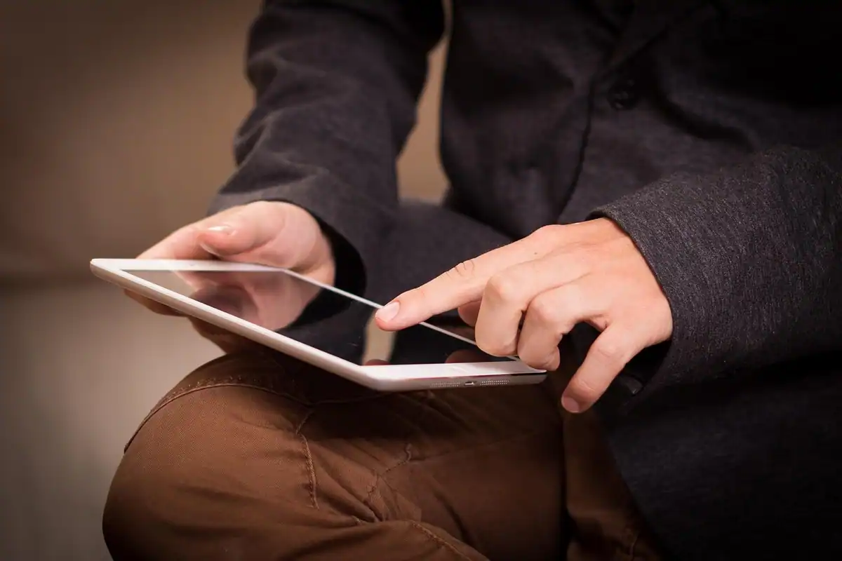 Mâini care derulează pe o tabletă ținută în poală