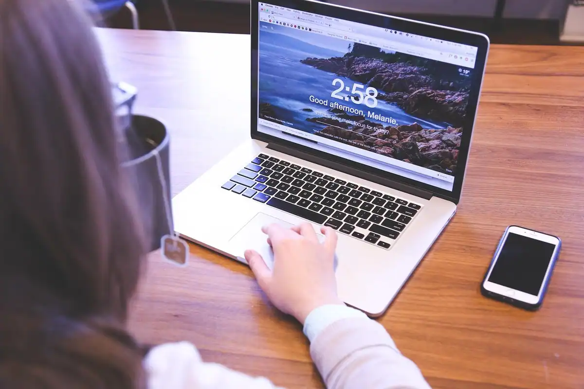 Femeie care lucrează la laptop, cu un telefon așezat pe masă