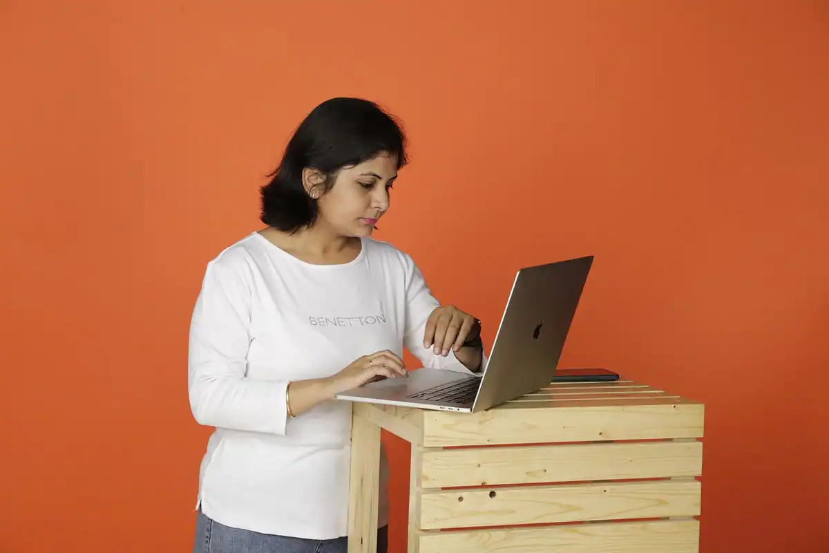 Femeie care lucrează la laptop, pe o masă de lemn